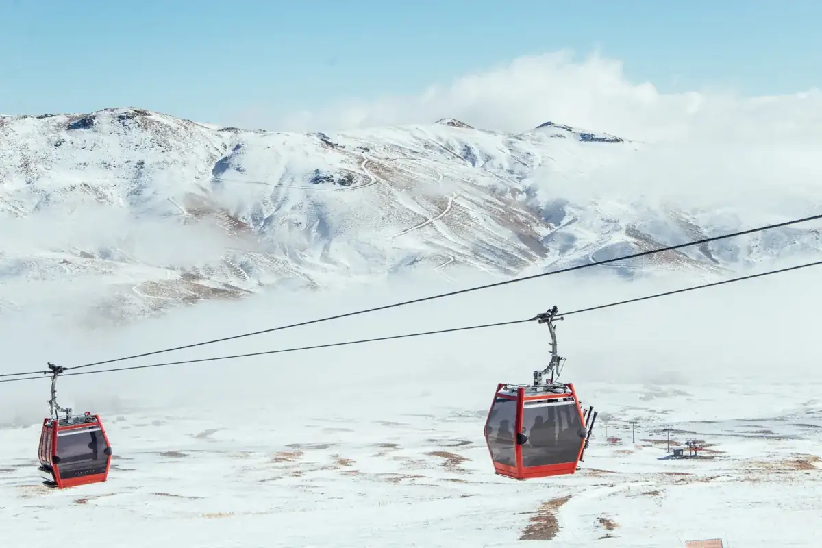 Erciyes Kayak Merkezi’nde karla kaplı yamaçların önünden geçen kırmızı gondol kabinleri
