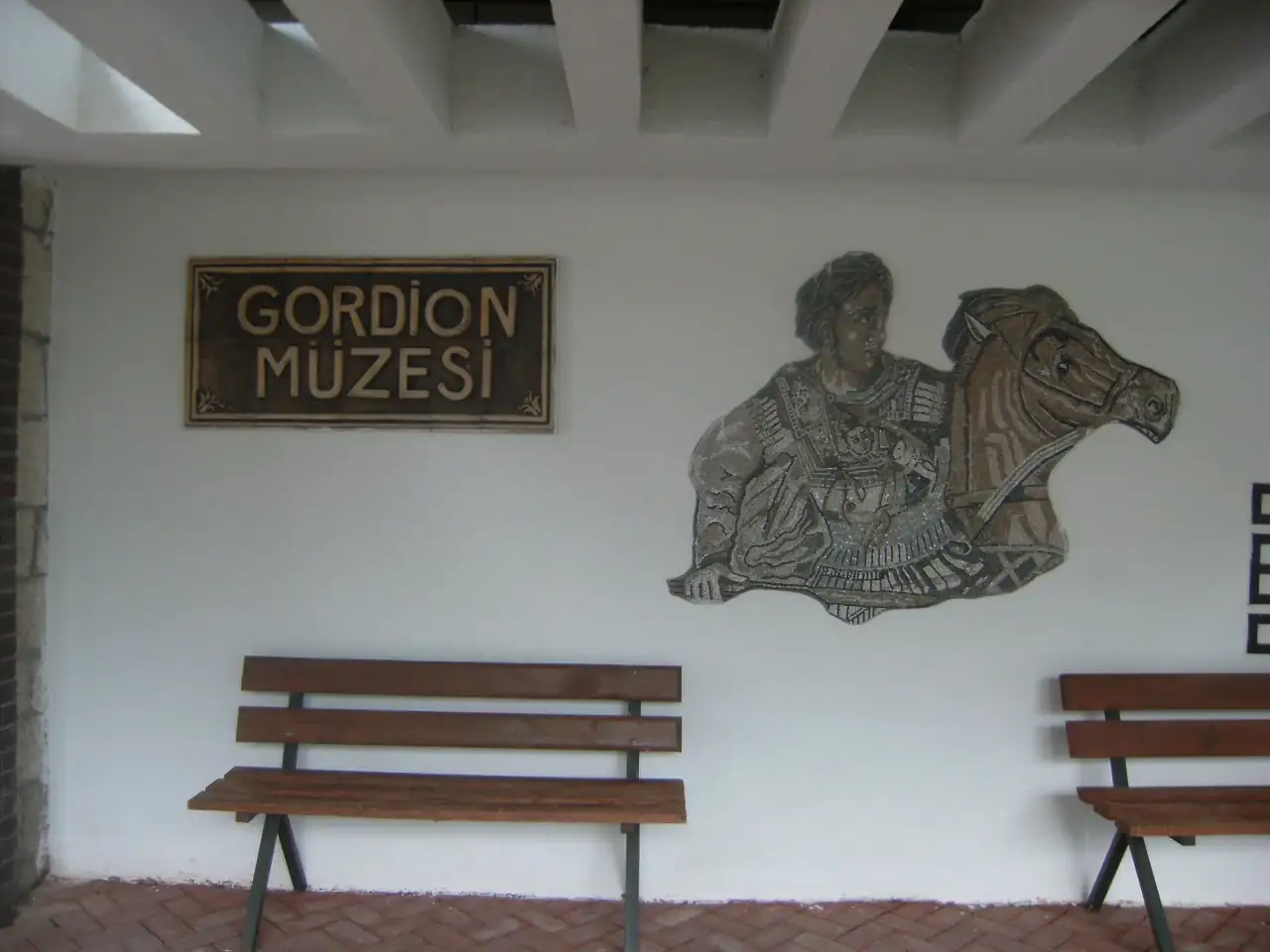 Gordion Müzesi yazılı tabelanın, atlı figürlü duvar bezemesinin ve ahşap bankların bulunduğu giriş bölümü