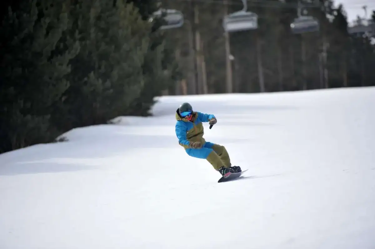 Sarıkamış Kayak Merkezi’nde çam ağaçları ve telesiyej önündeki karlı pistte snowboard yapan sporcu