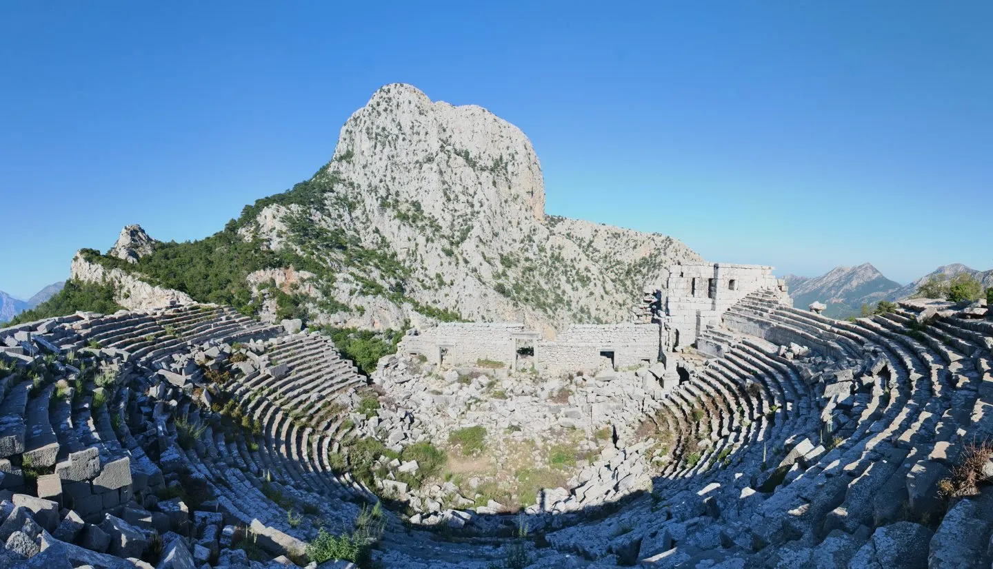 Termessos antik tiyatrosunun taş oturma sıraları ve arkadaki dağ silueti