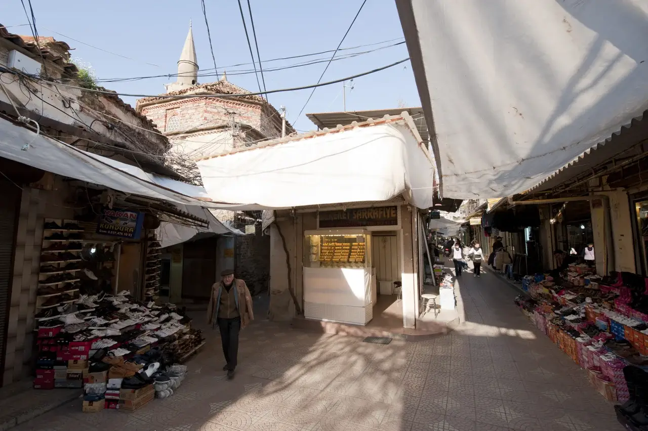 Tire çarşısında dükkânlar ve tenteler arasından görünen Hasır Pazarı Camii minaresi