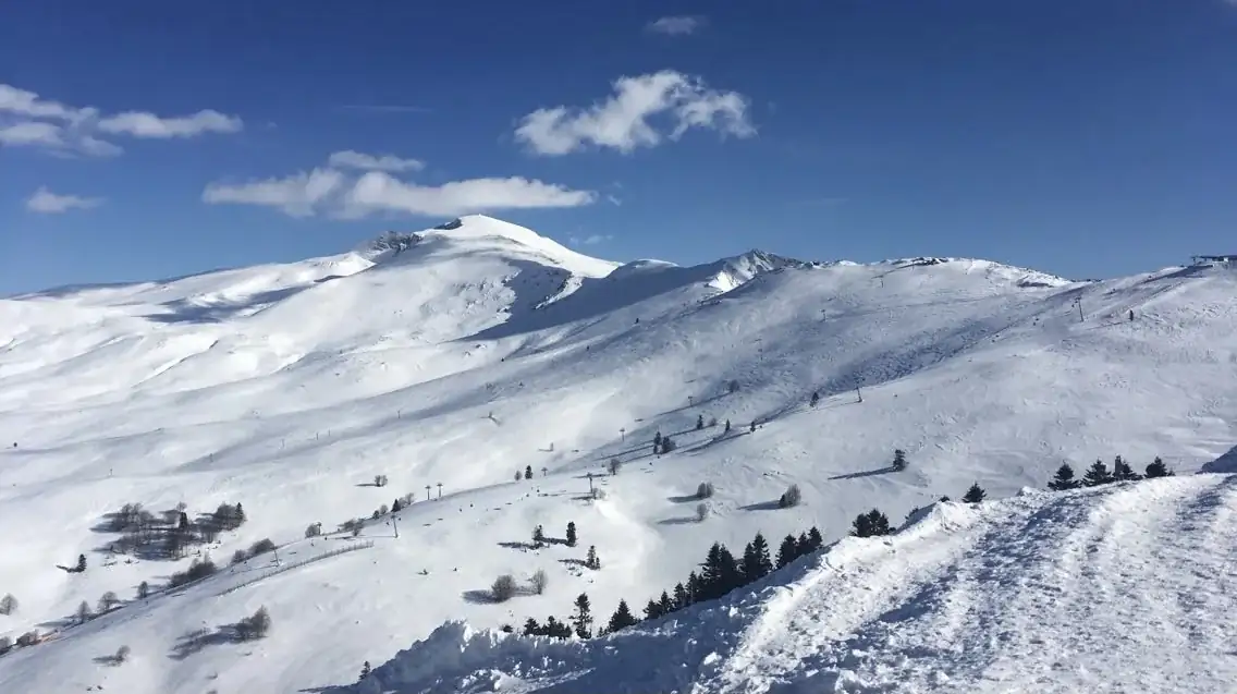 Uludağ’da mavi gökyüzü altında karla kaplı dağ sırtları ve seyrek ağaçlar